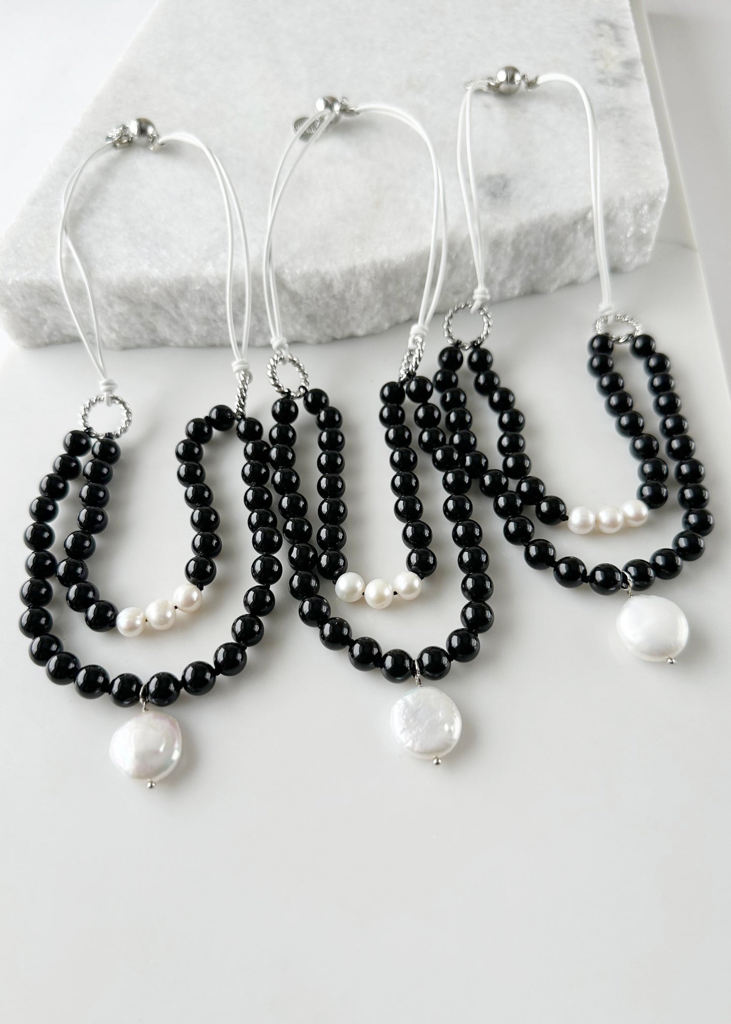White Freshwater and Coin Pearl Drop on Two Strand Necklace with Black Agate and White Leather.  A strong secure Magnetic Clasp Allows for Easy Wear. Three Shown