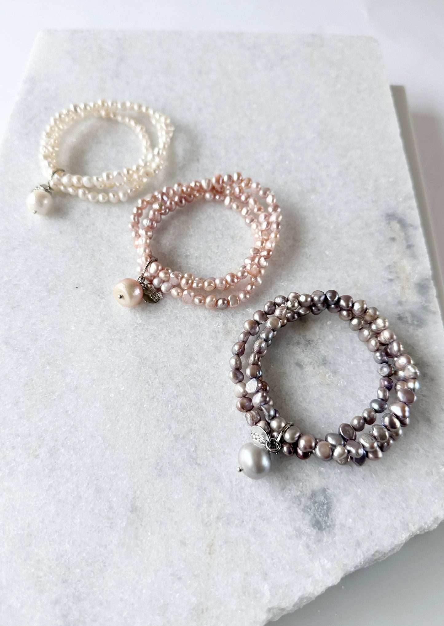 Three Strands of Delicate Baroque Freshwater Pearls with a Large Pearl Dangle form this Pretty Stretch Bracelet. Three Color Options are shown: White, Pink and Silver.