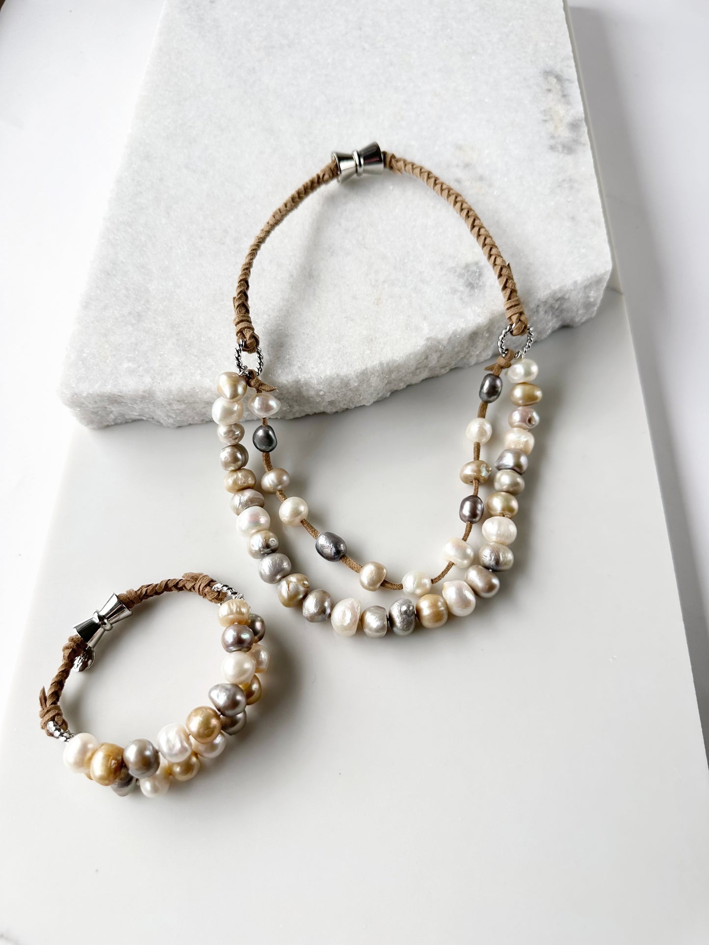 This 8” Bracelet has Two Knotted Strands of Large Freshwater Pearls with Braided Vegan Suede Accented with Silver Rings and a Magnetic Clasp. Designed in Canada