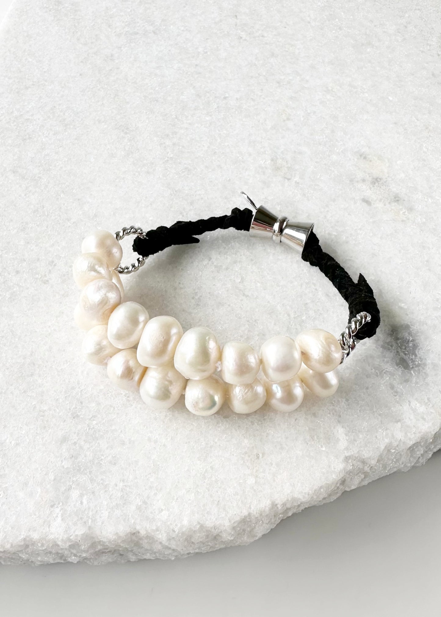 This 8” Bracelet has Two Knotted Strands of Large Freshwater Pearls with Braided Vegan Suede Accented with Silver Rings and a Magnetic Clasp. Designed in Canada