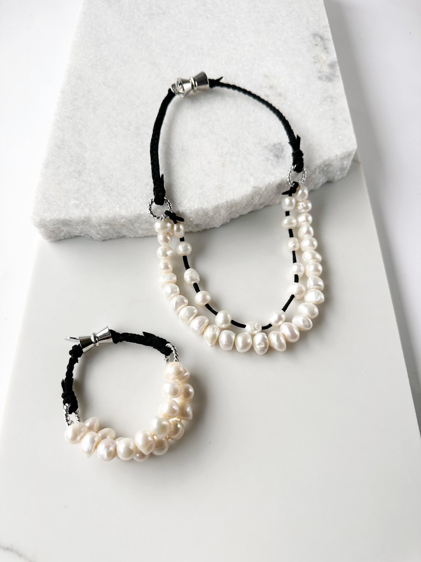 This 8” Bracelet has Two Knotted Strands of Large Freshwater Pearls with Braided Vegan Suede Accented with Silver Rings and a Magnetic Clasp. Designed in Canada