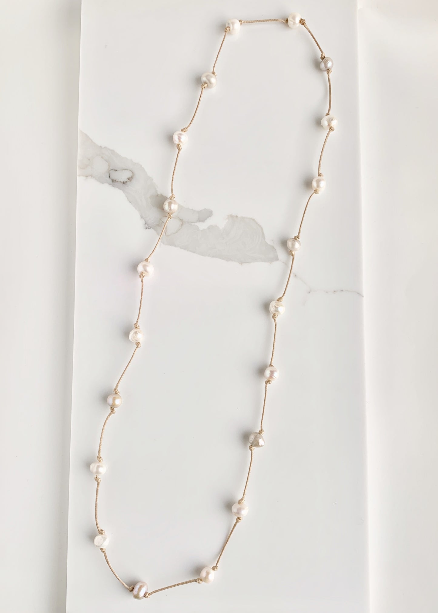 Lustrous White Freshwater Pearls Knotted on Beige Cotton in this 21” Necklace.