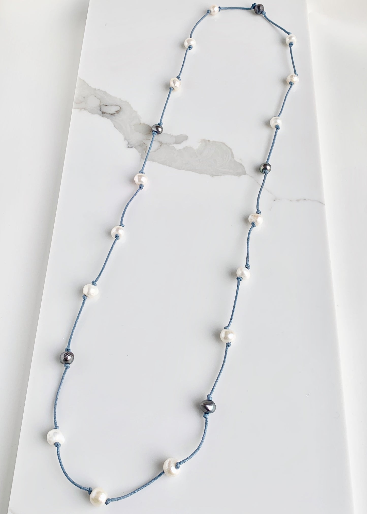 Lustrous White and Silver Freshwater Pearls Knotted on Blue Cotton in this 21” Necklace.