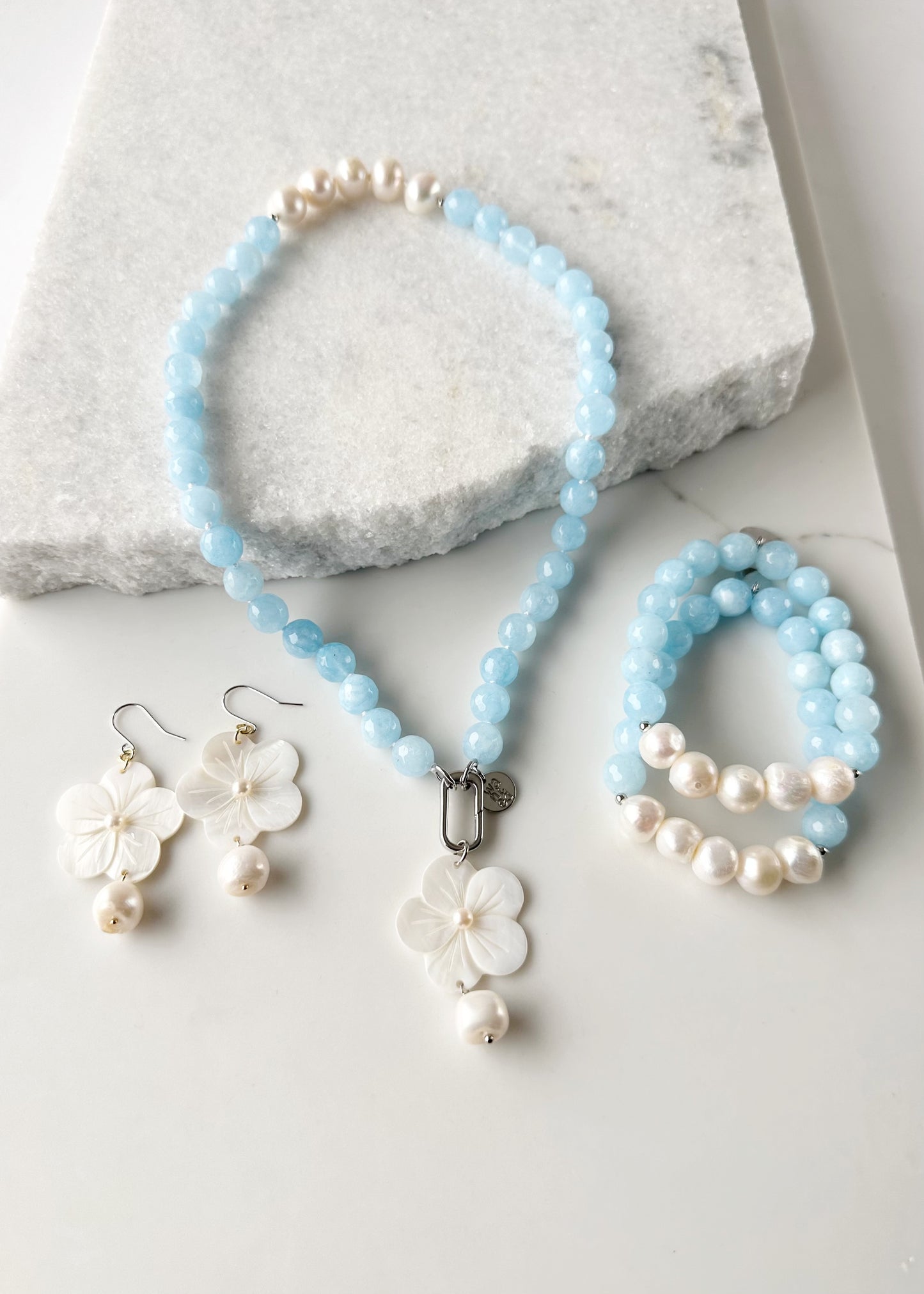 Five Large White Baroque Freshwater Pearls Accompanied by Light Blue Semi-Precious Stones (10 mm) with Silver accents in this 7” Stretch Bracelet. Matching Flora Necklace and Farrah Earrings also shown.