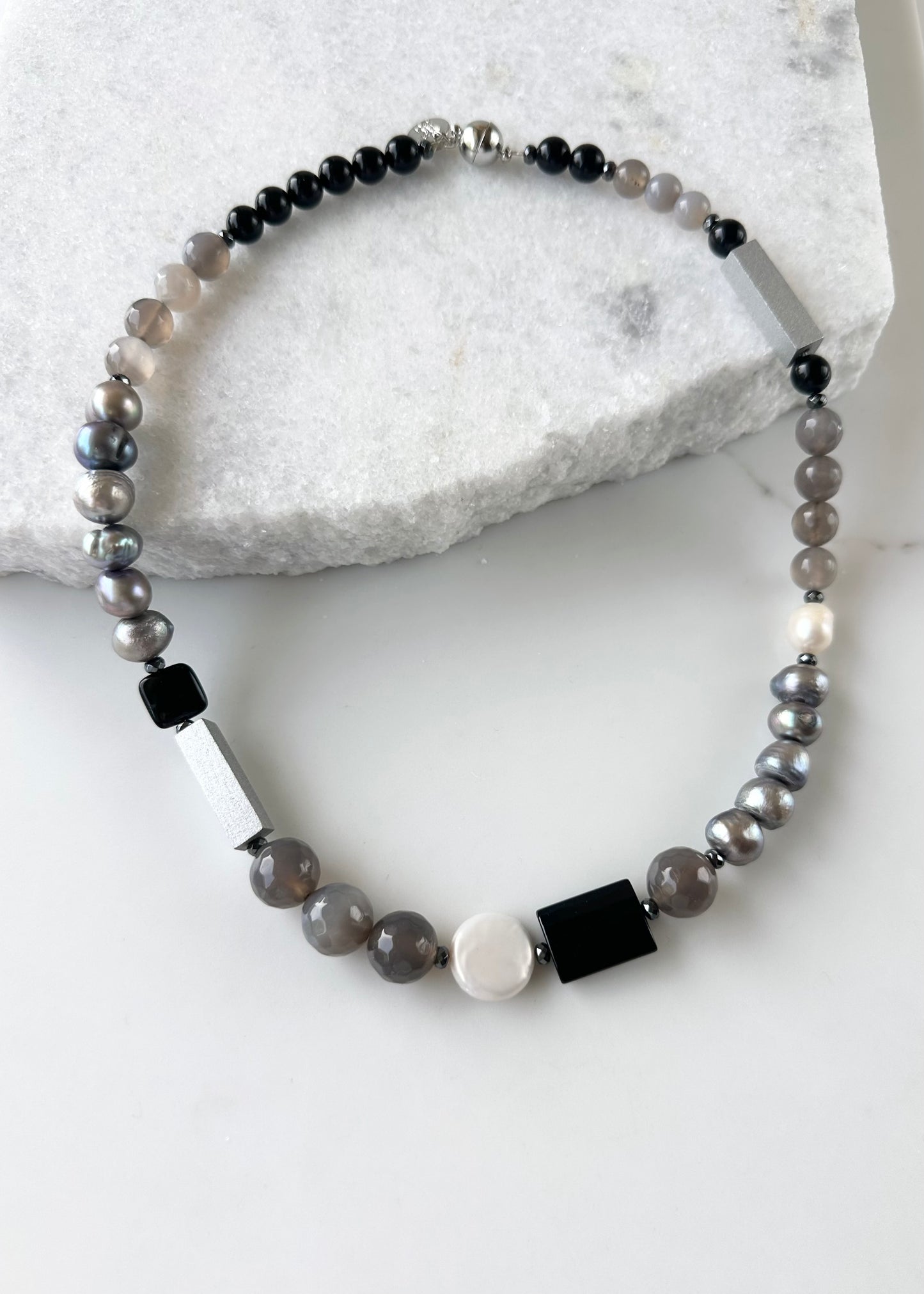 This Limited Edition 21” Necklace, Features Silver and White Freshwater Pearls Complemented by Striking Black Onyx, Silver Wood, Hematite and Soothing Grey Agate. A Magnetic Clasp offers simple, reliable attachment. This unique blend offers a bold yet elegant necklace that enhances any outfit and highlights your distinctive style. Designed and made in Canada