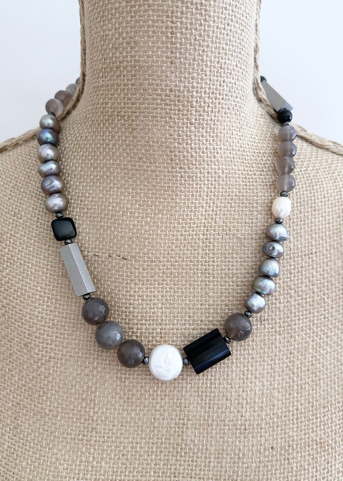 This Limited Edition 21” Necklace, Features Silver and White Freshwater Pearls Complemented by Striking Black Onyx, Silver Wood, Hematite and Soothing Grey Agate. A Magnetic Clasp offers simple, reliable attachment. This unique blend offers a bold yet elegant necklace that enhances any outfit and highlights your distinctive style. Designed and made in Canada