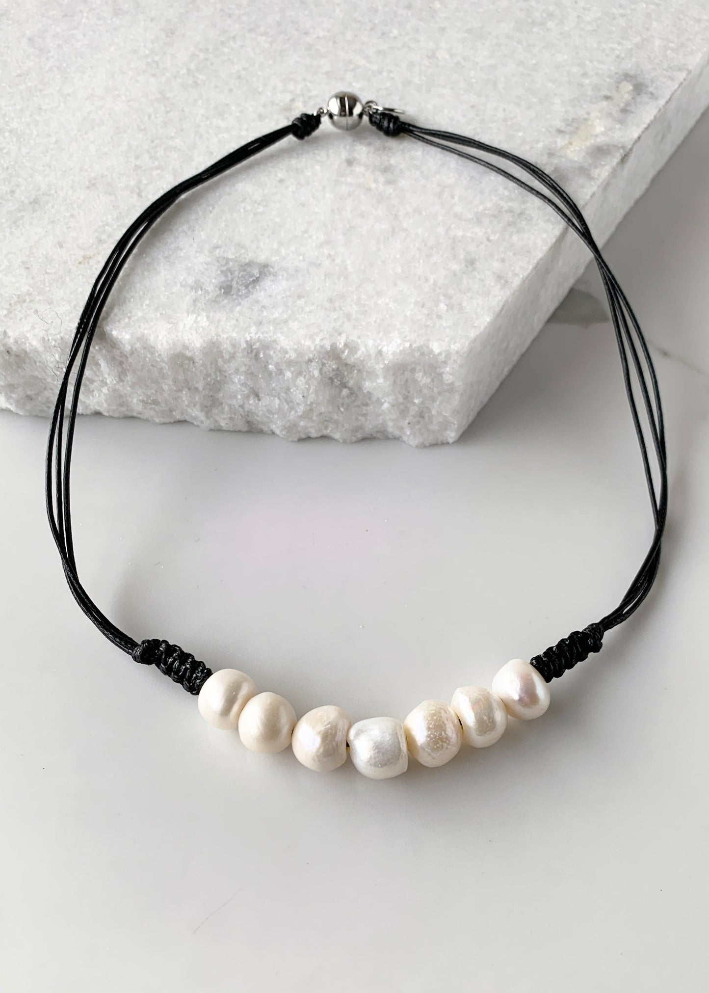 Seven Lustrous White Freshwater Baroque Pearls set on Black Cotton Cord with a Hint of Decorative Knotting on this 20” Necklace.