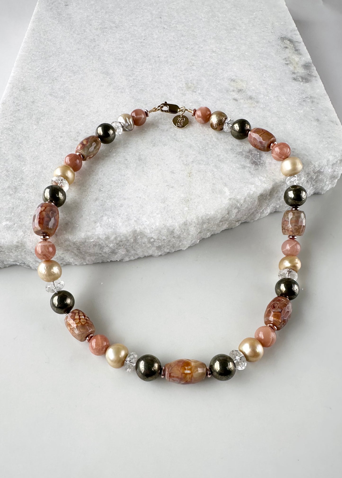 Designed and made in Canada, this beautiful One-Of-A-Kind 18.5” Necklace has Peach/Gold Tones with Faceted Agate Barrels, Large Pyrite Rounds, Faceted Clear Quartz, Moonstone and Lustrous Gold Freshwater Pearls. This piece is Finished with Gold-filled Lobster Claw Clasp and Rose Gold-Plated Hematite.