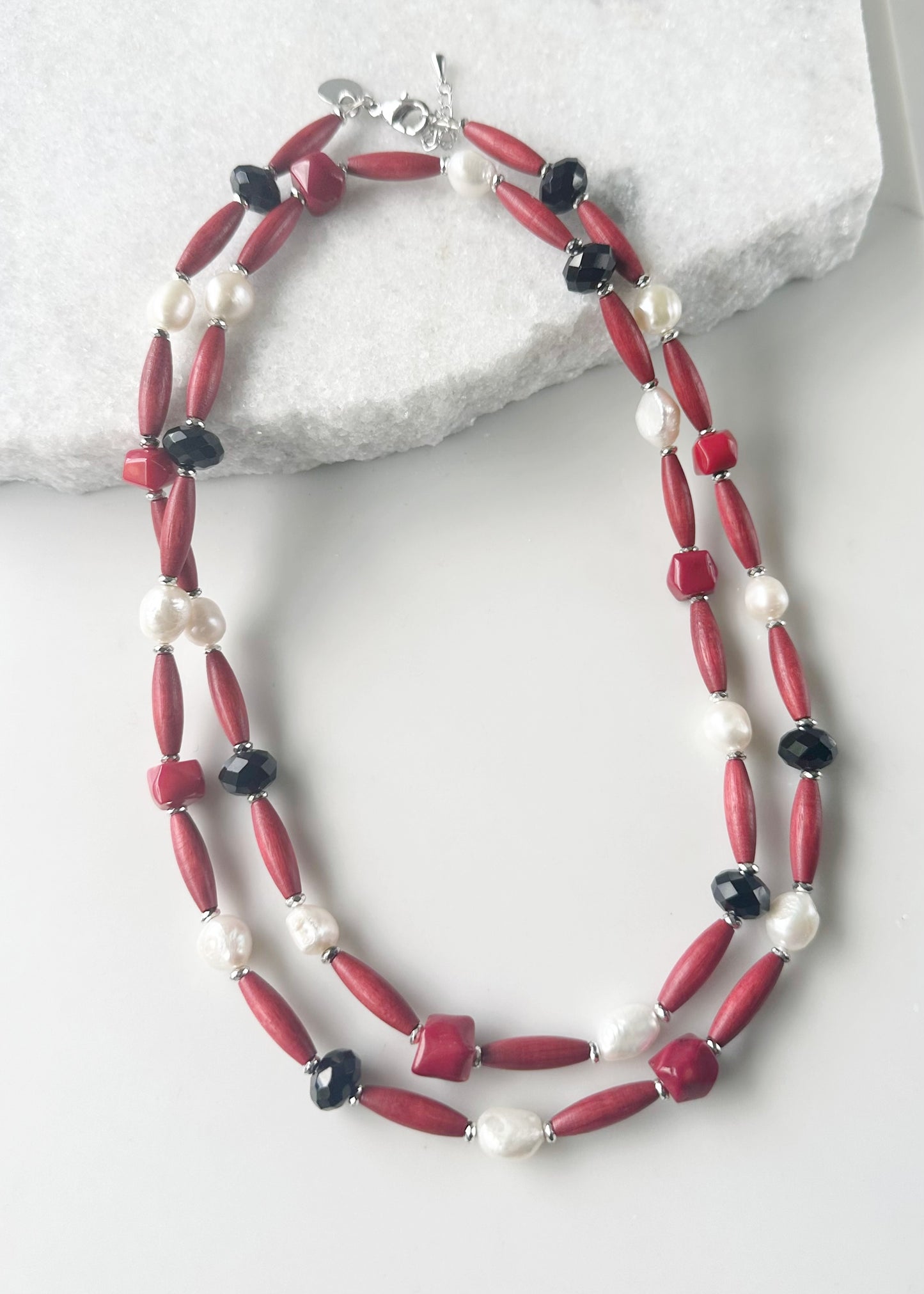Designed and Made in Canada, this One-Of-A-Kind 40” Necklace Combines Red Bamboo Coral Nuggets, Faceted Black Crystals, Warm Red Wood, and Lustrous White Freshwater Pearls. The piece is Accented with Silver Hematite for depth and Finished with a Lobster Claw Clasp and 1.5