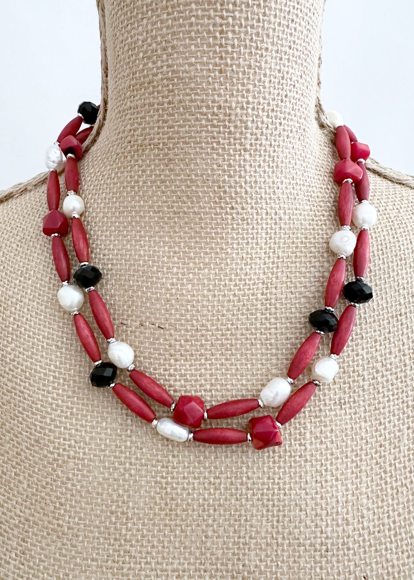 Designed and Made in Canada, this One-Of-A-Kind 40” Necklace Combines Red Bamboo Coral Nuggets, Faceted Black Crystals, Warm Red Wood, and Lustrous White Freshwater Pearls. The piece is Accented with Silver Hematite for depth and Finished with a Lobster Claw Clasp and 1.5