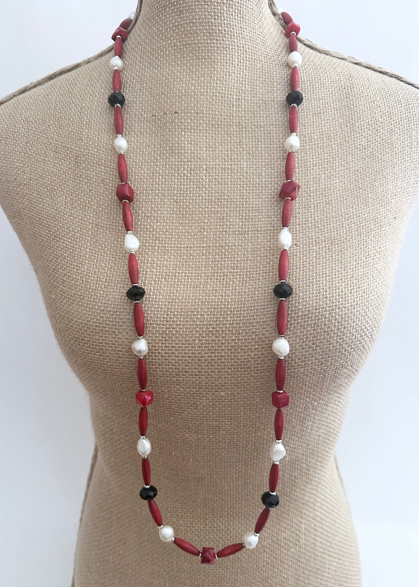 Designed and Made in Canada, this One-Of-A-Kind 40” Necklace Combines Red Bamboo Coral Nuggets, Faceted Black Crystals, Warm Red Wood, and Lustrous White Freshwater Pearls. The piece is Accented with Silver Hematite for depth and Finished with a Lobster Claw Clasp and 1.5