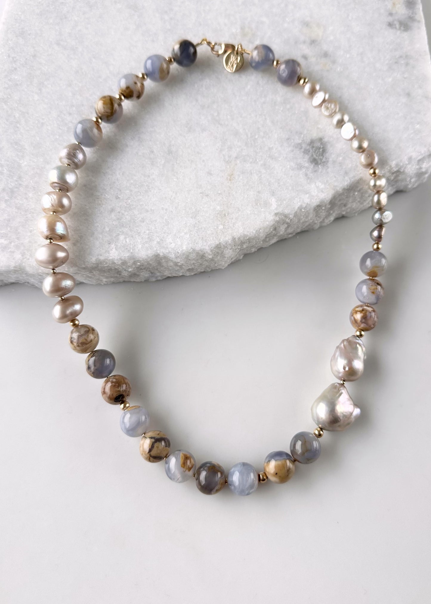 This Beautiful One-Of-A-Kind 21” Necklace features Serene 12mm Blue Chalcedony and Champagne Baroque Pearls. Gold accents and an Asymmetrical Design make this piece elegant and unique. Designed and made in Canada, this piece is Completed with a Gold-Filled Lobster Claw Clasp.