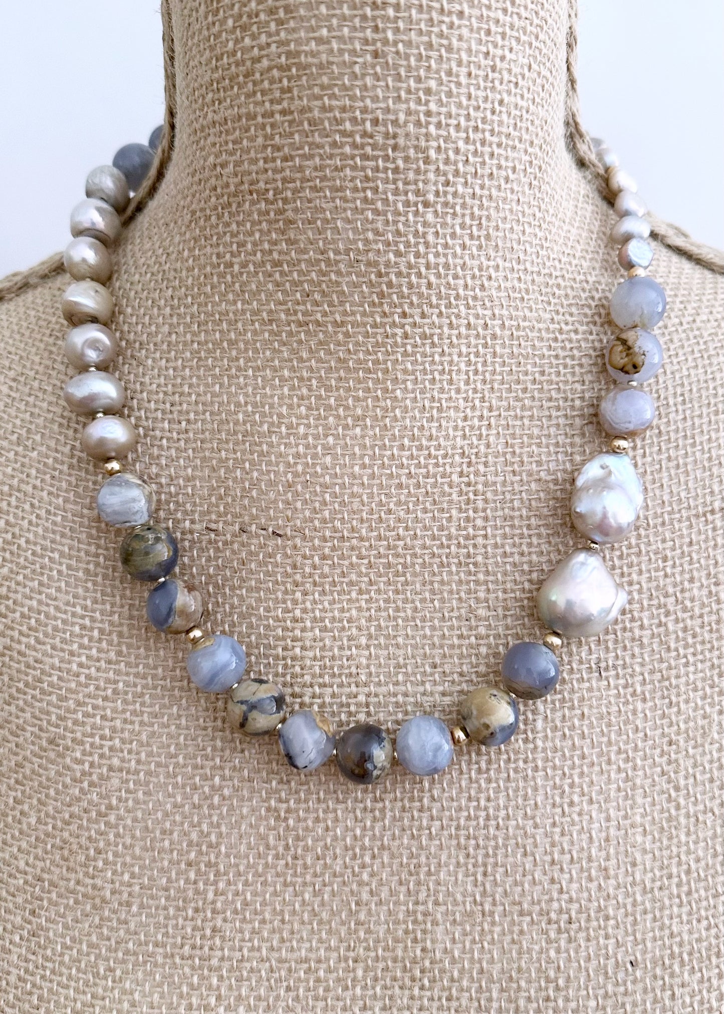 This Beautiful One-Of-A-Kind 21” Necklace features Serene 12mm Blue Chalcedony and Champagne Baroque Pearls. Gold accents and an Asymmetrical Design make this piece elegant and unique. Designed and made in Canada, this piece is Completed with a Gold-Filled Lobster Claw Clasp.