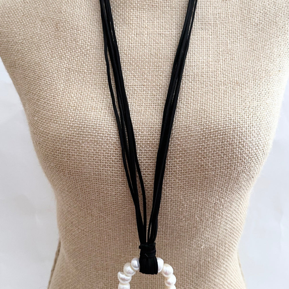 
                      
                        Necklace in Black Vegan Suede Displaying a Large Ring Pendant of White Freshwater Pearls. On Bust
                      
                    