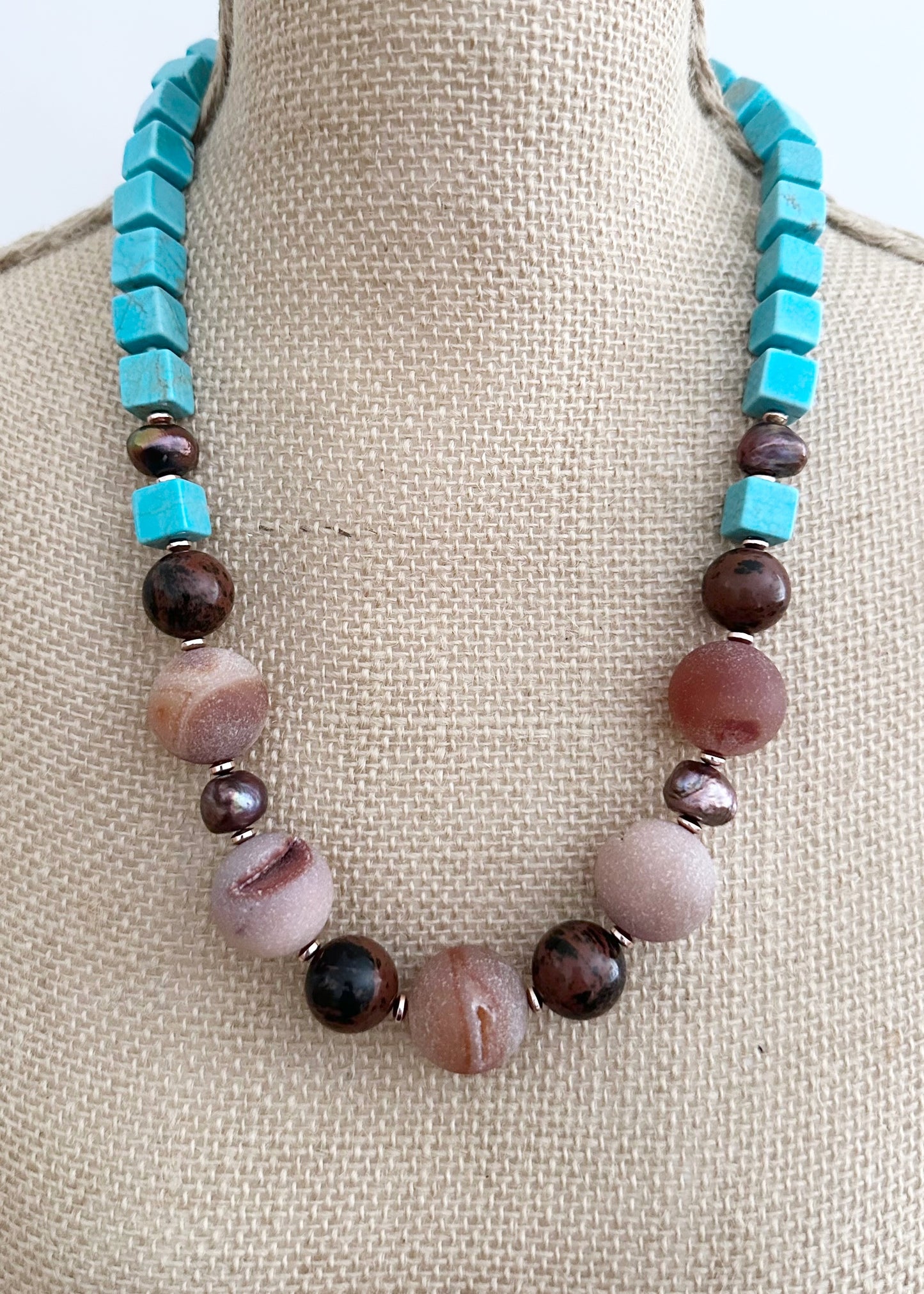 Designed and made in Canada, this One-Of-A-Kind 24” Necklace features Large Round Druzy Agate, Mahogany Obsidian, Turquoise Magnesite and Beautiful Brown Pearls. This piece is completed with Glass Seed Beads, Rose Gold-Plated Hematite and a Copper Toggle Clasp.