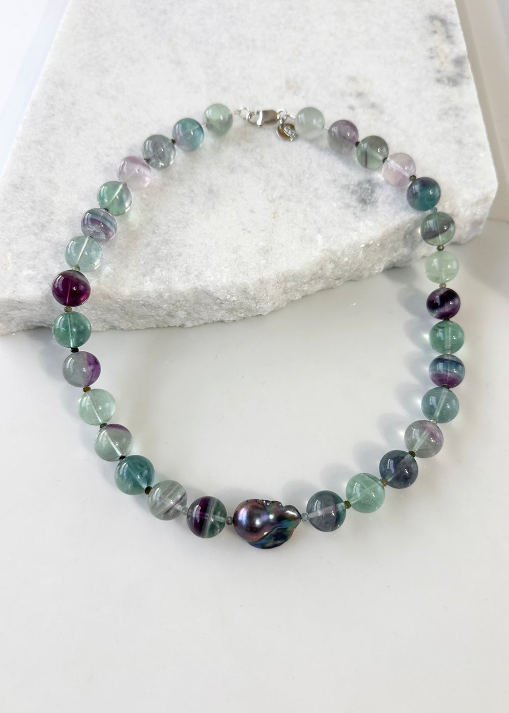 Designed and Made in Canada, this unique 20.5” Necklace features Striking Large Round Fluorite, Delicate Faceted Tourmaline, and a Stunning Peacock Baroque Pearl, creating an exquisite blend of vibrant colours. The piece is finished with a Sterling Silver Lobster Claw Clasp.