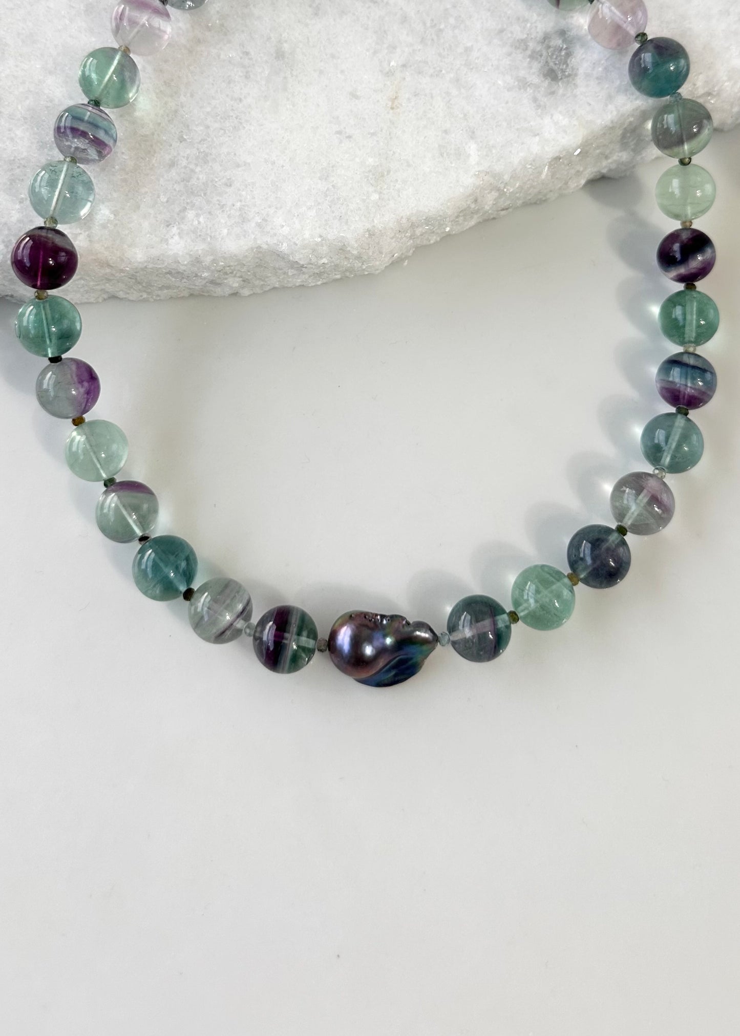Designed and Made in Canada, this unique 20.5” Necklace features Striking Large Round Fluorite, Delicate Faceted Tourmaline, and a Stunning Peacock Baroque Pearl, creating an exquisite blend of vibrant colours. The piece is finished with a Sterling Silver Lobster Claw Clasp.