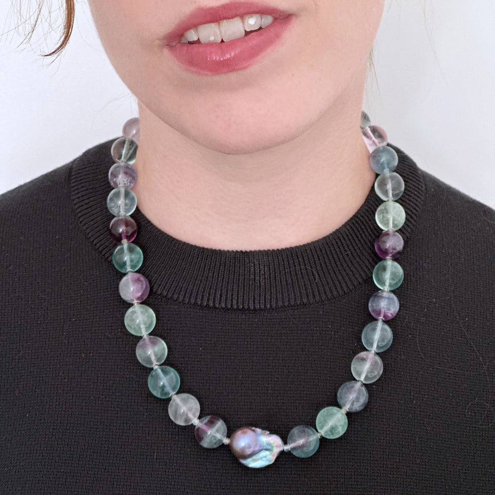 Designed and Made in Canada, this unique 20.5” Necklace features Striking Large Round Fluorite, Delicate Faceted Tourmaline, and a Stunning Peacock Baroque Pearl, creating an exquisite blend of vibrant colours. The piece is finished with a Sterling Silver Lobster Claw Clasp.