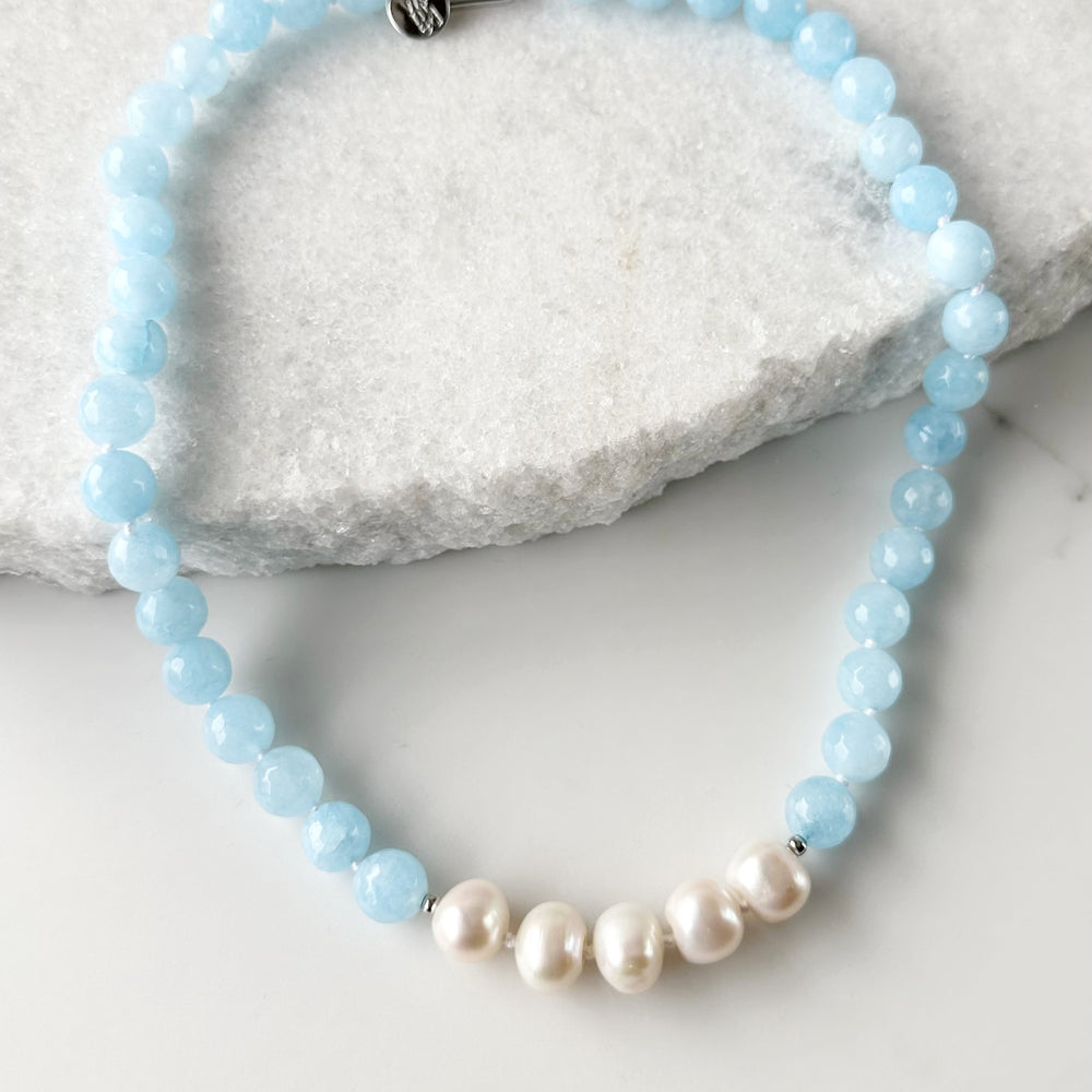
                      
                        White Freshwater Baroque Pearls Strung with Faceted White or Blue Semi-Precious Stones with a Pretty Carved Shell Flower Pendant Hanging from a Gold-Plated Rectangular Clasp for a 18.5” Necklace.  This Necklace can be worn in Various ways. Shown without Pendant.
                      
                    