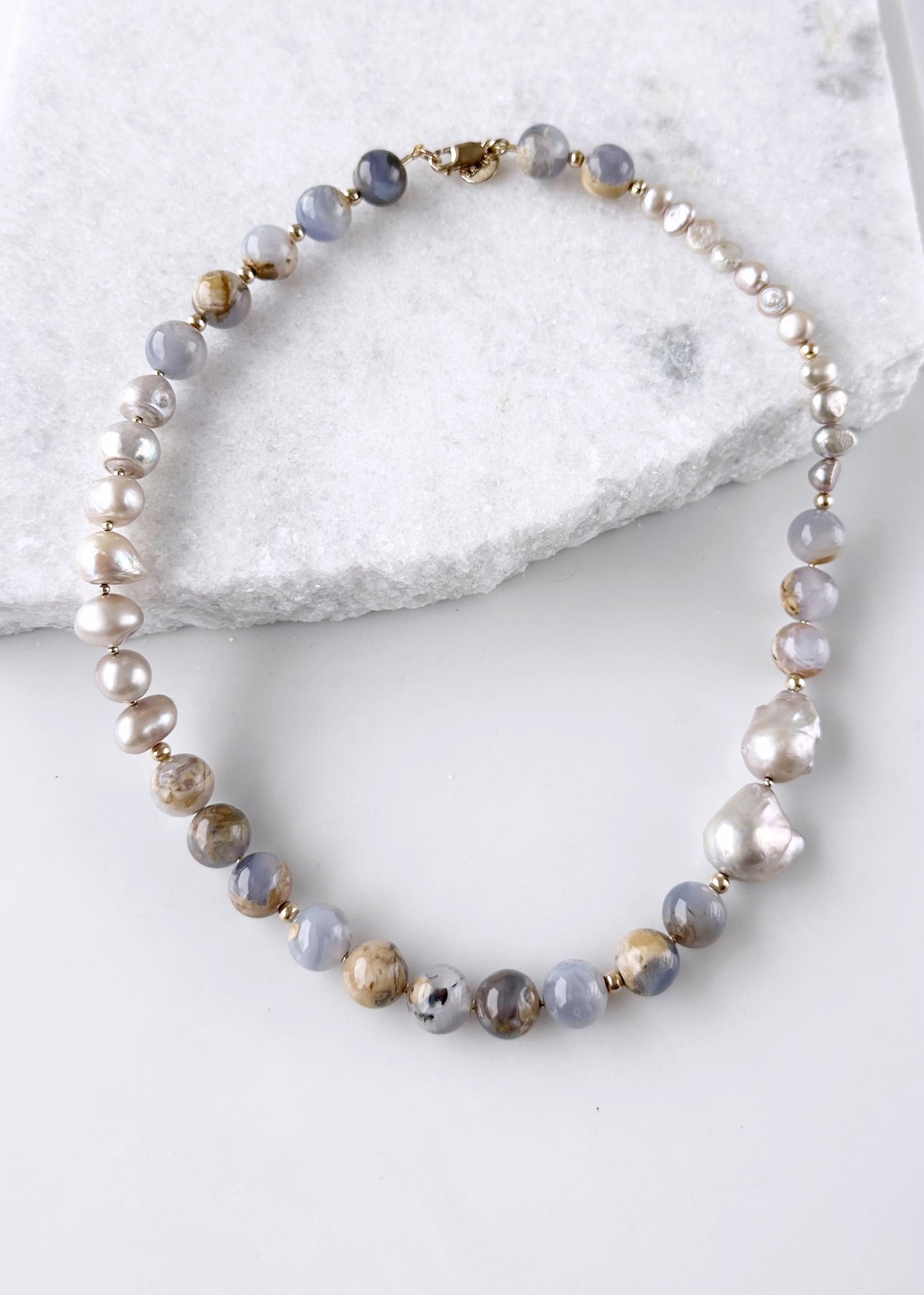This Beautiful One-Of-A-Kind 21” Necklace features Serene 12mm Blue Chalcedony and Champagne Baroque Pearls. Gold accents and an Asymmetrical Design make this piece elegant and unique. Designed and made in Canada, this piece is Completed with a Gold-Filled Lobster Claw Clasp.