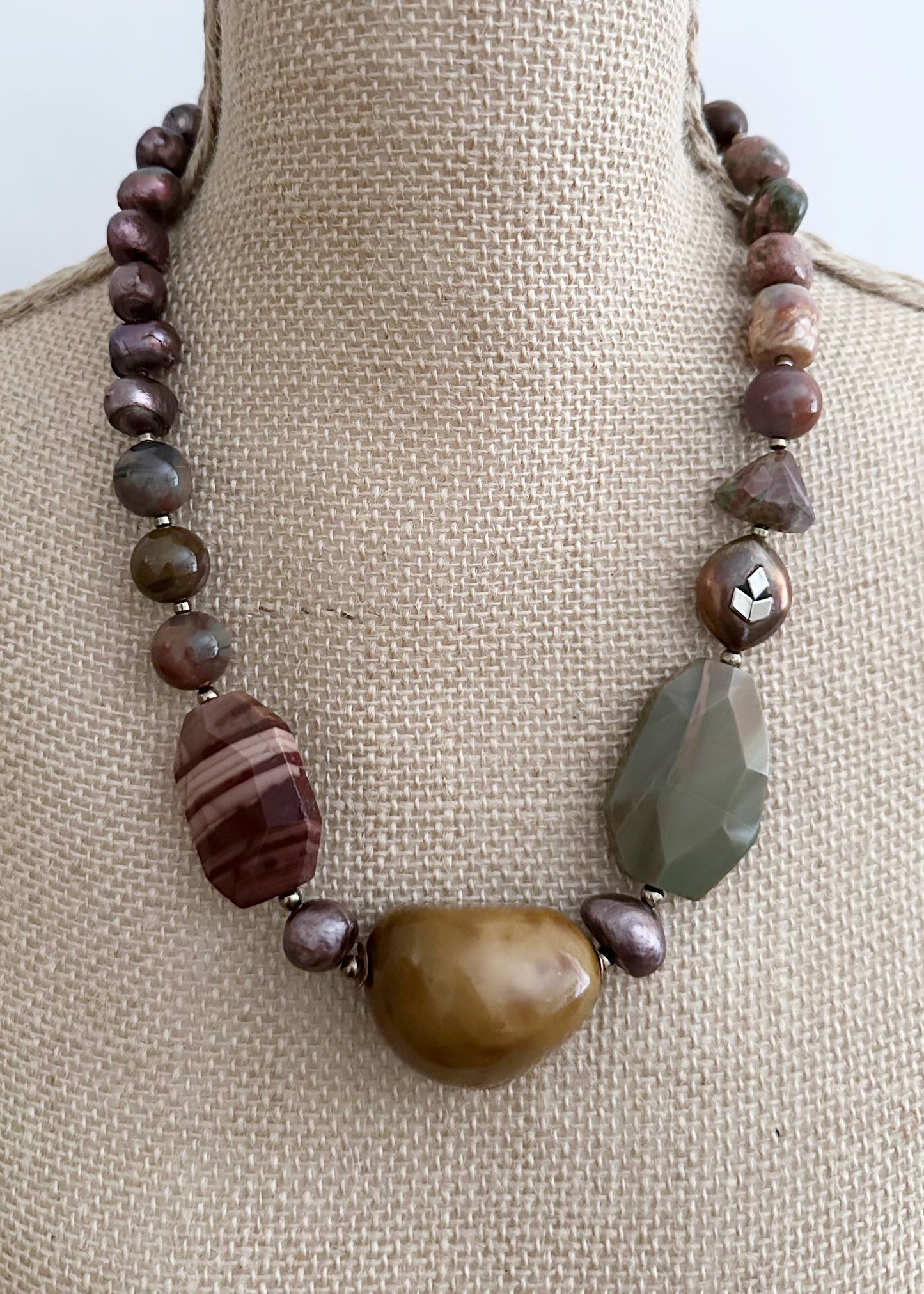 Designed and made in Canada, this Stunning One-Of-A-Kind 22.5" Necklace Showcases an Exquisite Blend of Imperial Jasper, Tagua Seed, Petrified Wood, Opalite, Unakite, and Agate, Accented with Lustrous Brown Pearls and Warm Copper and Gold details. Each element is thoughtfully combined to create a truly distinctive accessory that celebrates nature's palette and timeless elegance.