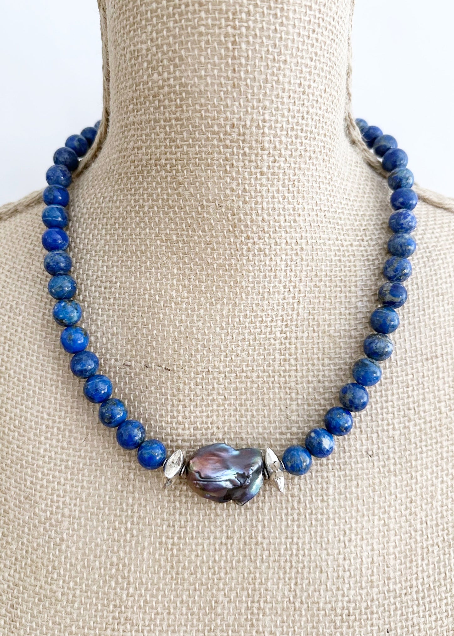 A Large Peacock Baroque Freshwater Pearl sits Center Stage amidst Silver Accents and Beautiful Blue Lapis Lazuli Beads on this One-Of-A-Kind 20” Necklace.  It is finished with a Sterling Silver Lobster Claw Clasp.