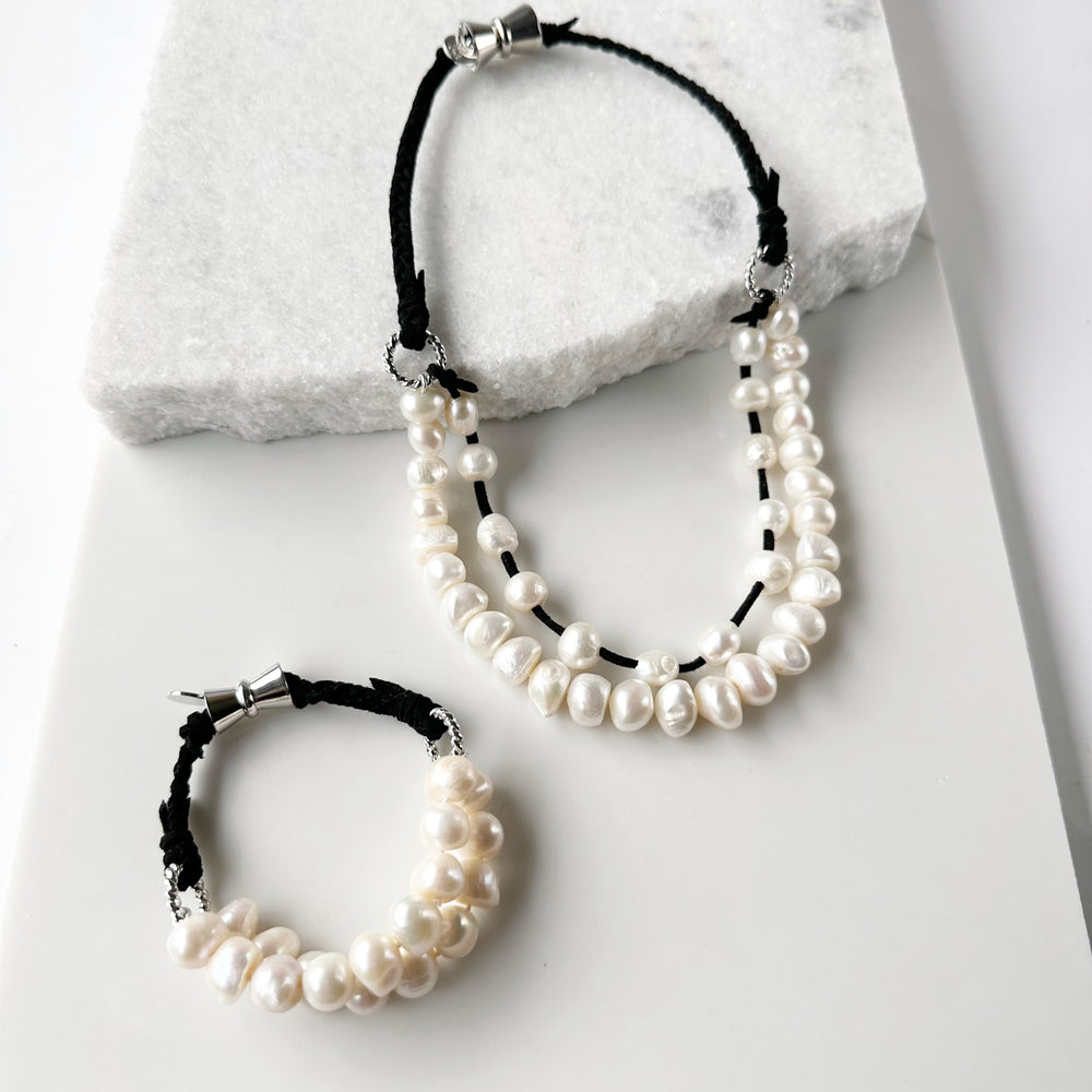 
                      
                        This 8” Bracelet has Two Knotted Strands of Large Freshwater Pearls with Braided Vegan Suede Accented with Silver Rings and a Magnetic Clasp. Designed in Canada
                      
                    