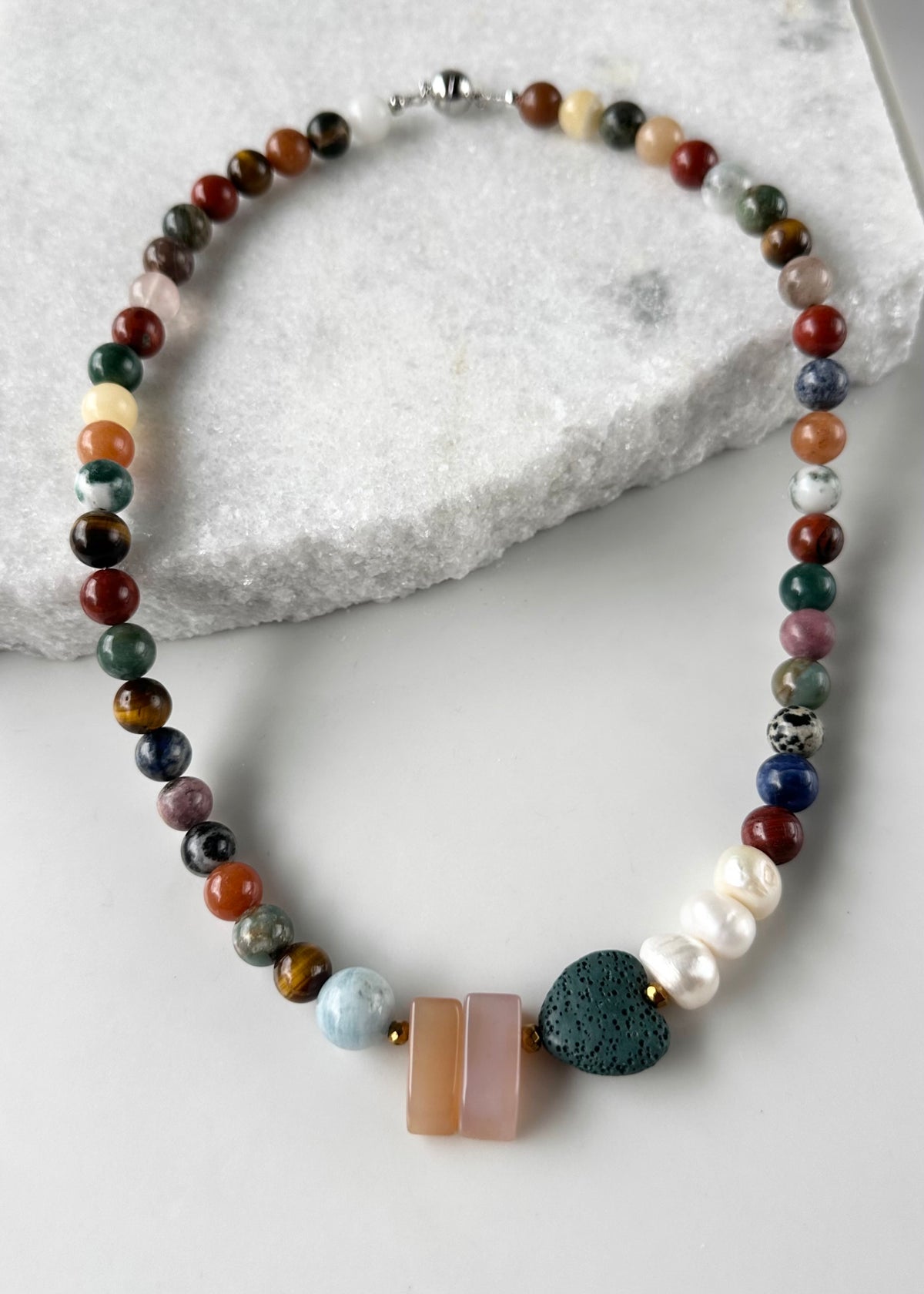 Designed and Made in Canada, this 22” Limited-Edition Necklace features a mix of round semi-precious stones in pretty Fall Shades highlighted by Aquamarine, Pink Chalcedony, a green Lava Stone Heart and 3 Lustrous Pearls finished with a Magnetic Clasp.