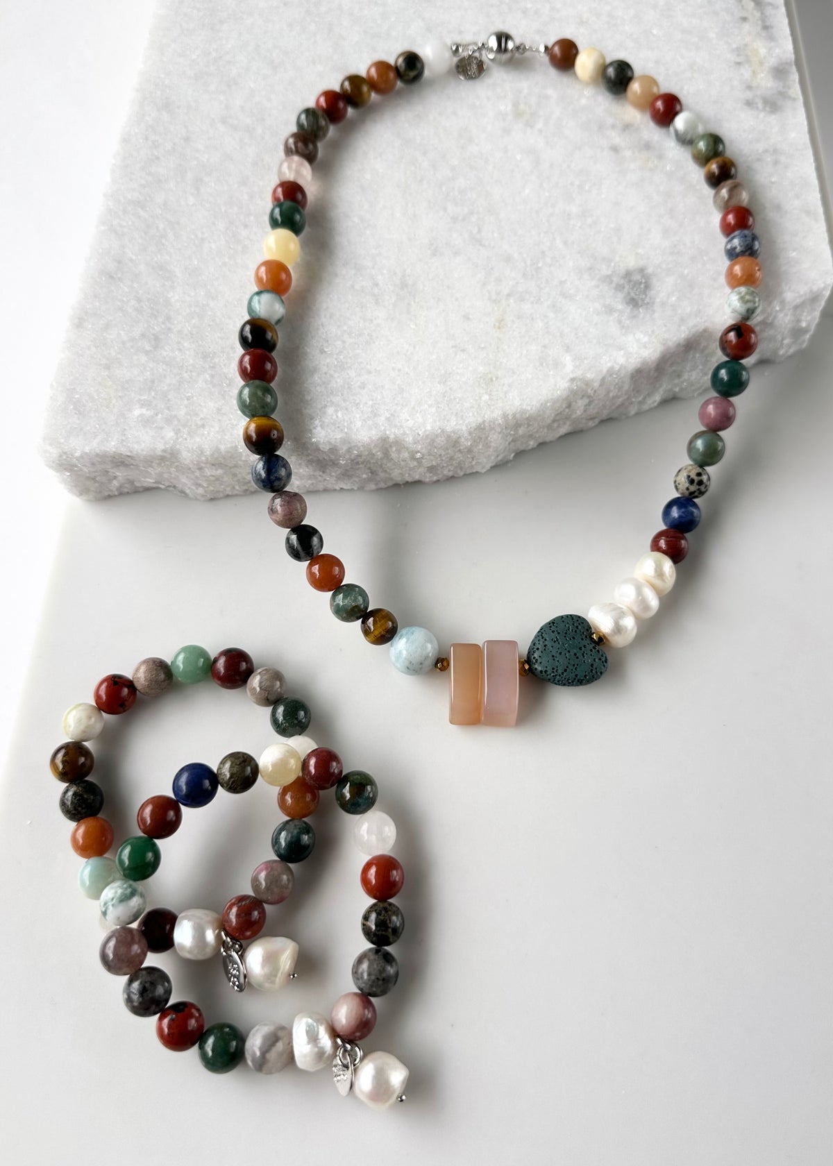 Designed and Made in Canada, this 22” Limited-Edition Necklace features a mix of round semi-precious stones in pretty Fall Shades highlighted by Aquamarine, Pink Chalcedony, a green Lava Stone Heart and 3 Lustrous Pearls finished with a Magnetic Clasp.