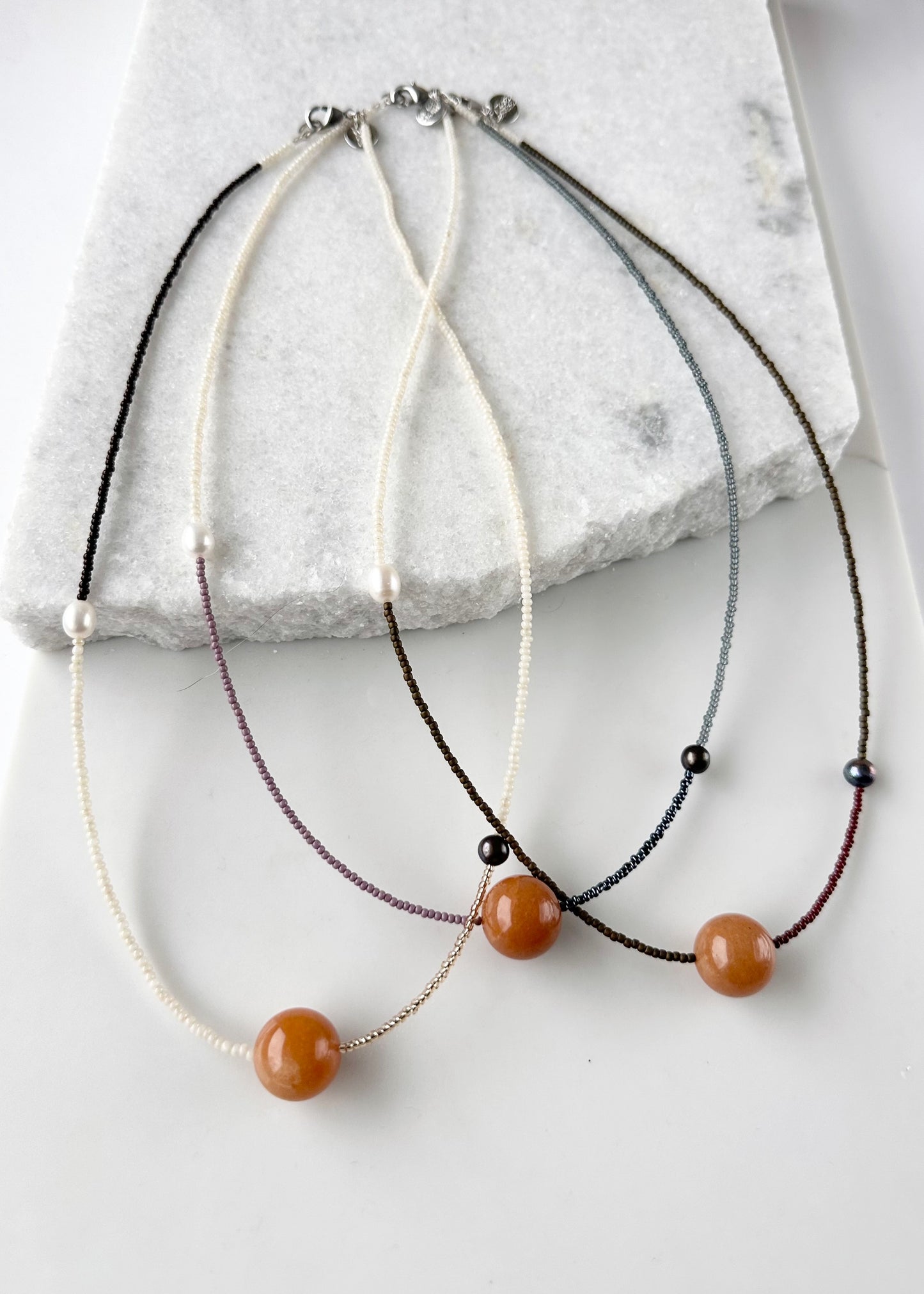 This 24.5” Necklace features Orange Aventurine (18mm), White and Black pearls, Glass Seed Beads in a Striking Asymmetrical Design. Designed and Made in Canada, to be wonderfully light and comfortable to wear, this Limited-Edition piece is completed with a Lobster Claw Clasp.