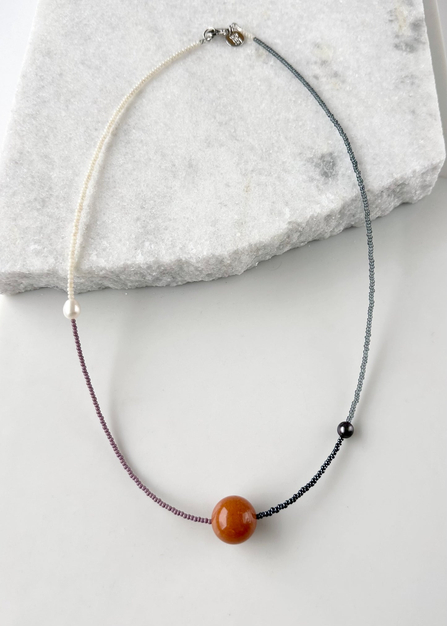 This 24.5” Necklace features Orange Aventurine (18mm), White and Black pearls, Glass Seed Beads in a Striking Asymmetrical Design. Designed and Made in Canada, to be wonderfully light and comfortable to wear, this Limited-Edition piece is completed with a Lobster Claw Clasp.