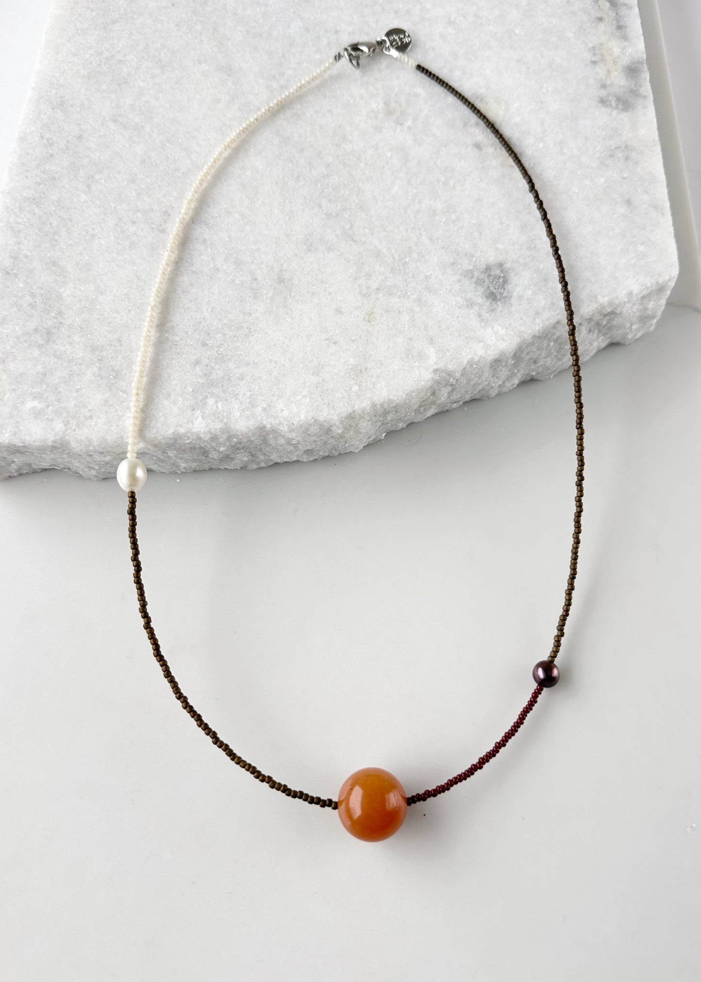 This 24.5” Necklace features Orange Aventurine (18mm), White and Black pearls, Glass Seed Beads in a Striking Asymmetrical Design. Designed and Made in Canada, to be wonderfully light and comfortable to wear, this Limited-Edition piece is completed with a Lobster Claw Clasp.