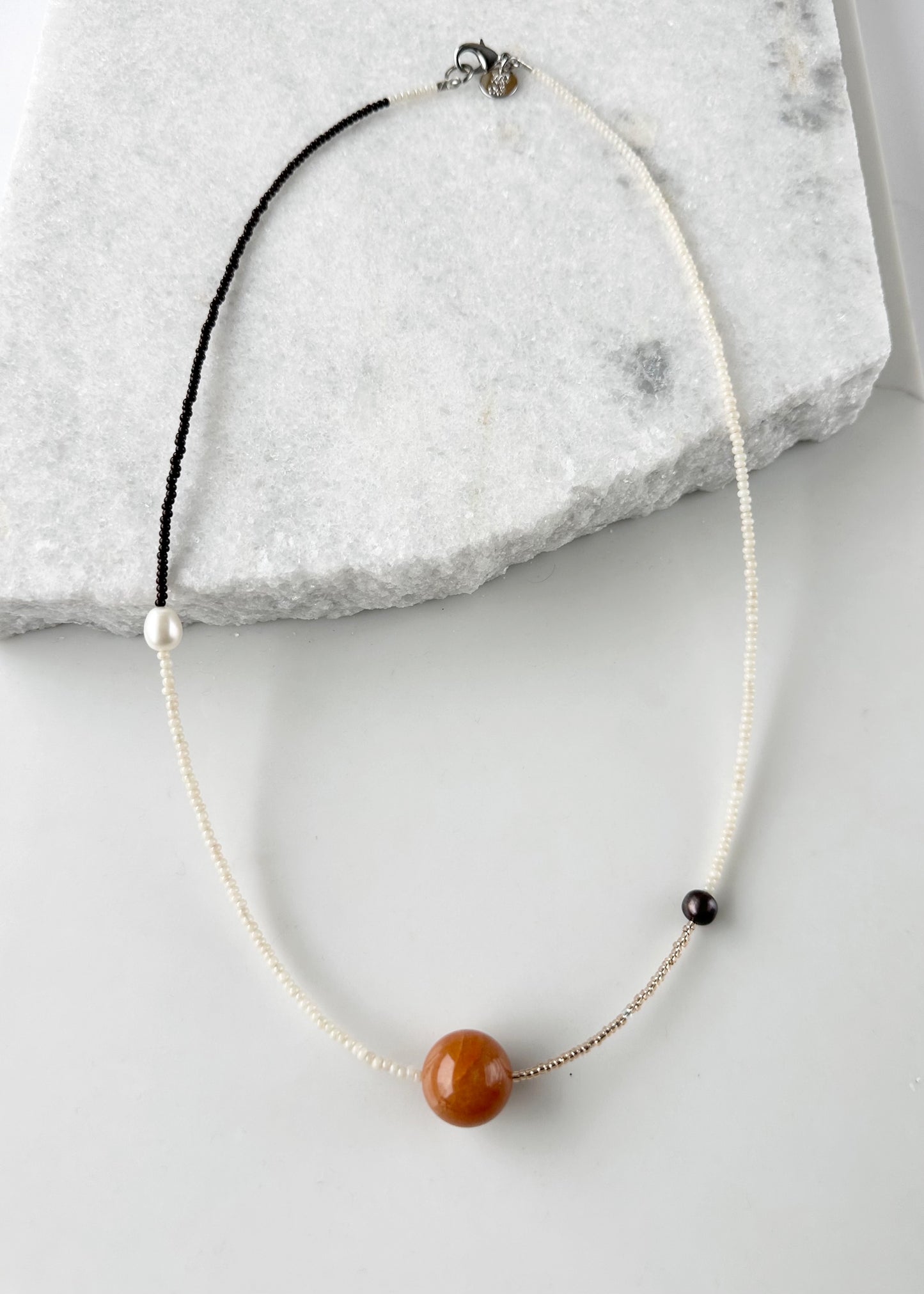 This 24.5” Necklace features Orange Aventurine (18mm), White and Black pearls, Glass Seed Beads in a Striking Asymmetrical Design. Designed and Made in Canada, to be wonderfully light and comfortable to wear, this Limited-Edition piece is completed with a Lobster Claw Clasp.
