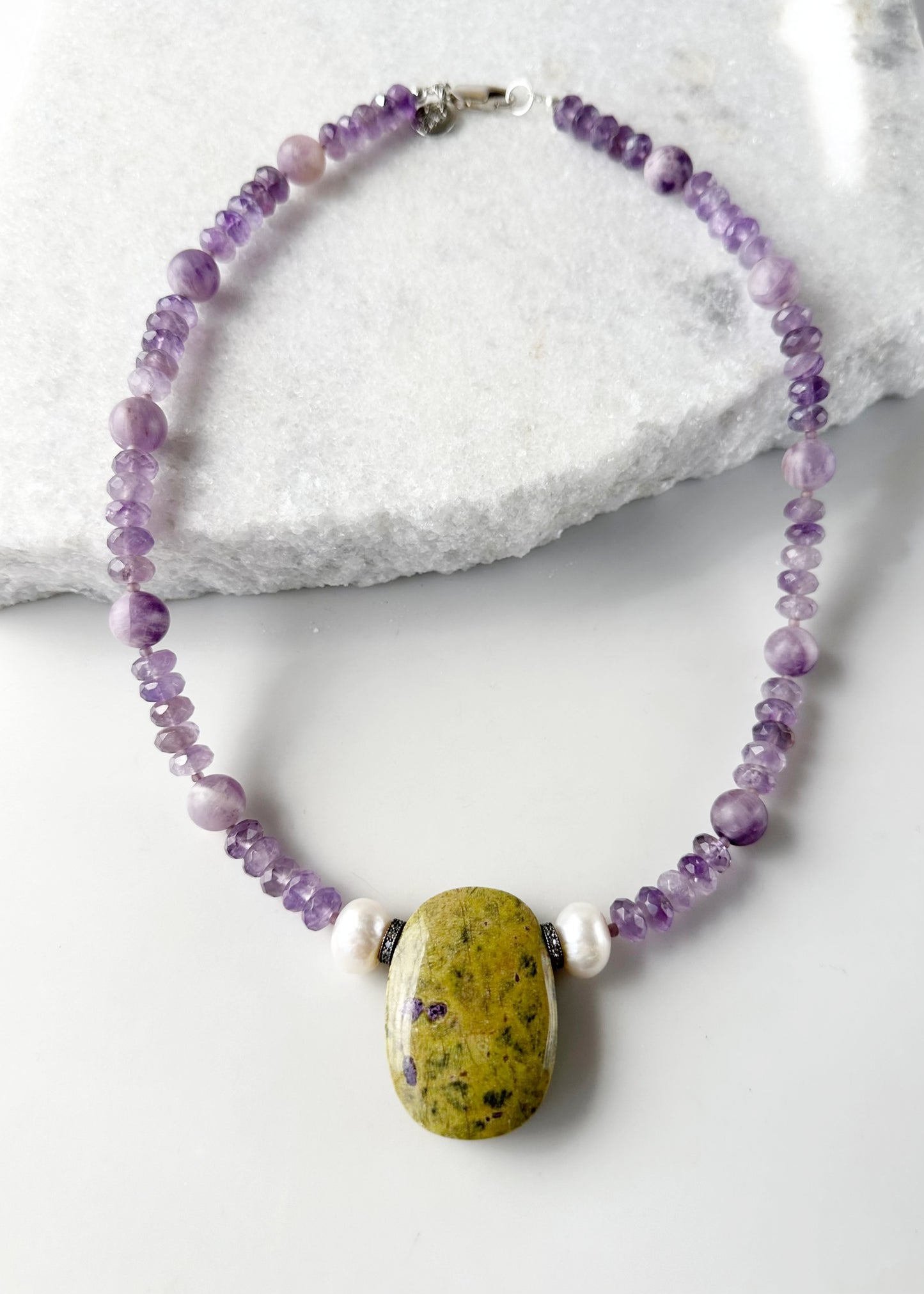 Designed and Made in Canada, this One-Of-A-Kind 20.5” Necklace features a large Stichtite Pendant, a Stunning Natural Stone known for its Purple and Green hues. Paired with Lustrous Freshwater Pearls, Faceted Amethyst and Matte Round Amethyst this piece combines elegance with organic charm.  This piece is finished with a Sterling Silver Lobster Claw Clasp.