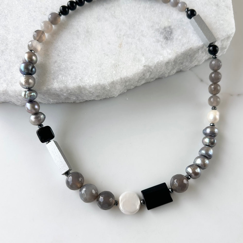 This Limited Edition 21” Necklace, Features Silver and White Freshwater Pearls Complemented by Striking Black Onyx, Silver Wood, Hematite and Soothing Grey Agate. A Magnetic Clasp offers simple, reliable attachment. This unique blend offers a bold yet elegant necklace that enhances any outfit and highlights your distinctive style. Designed and made in Canada