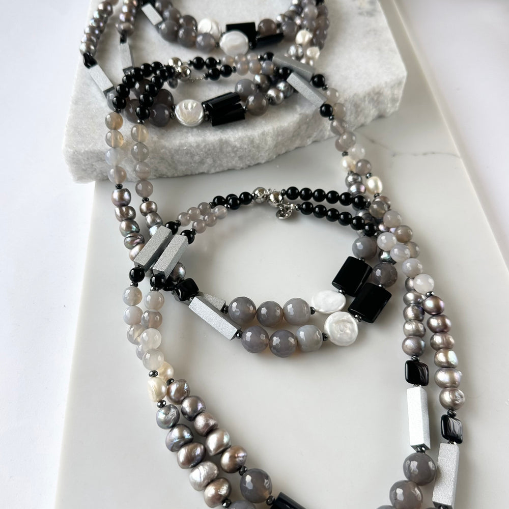 
                      
                        This Limited Edition 21” Necklace, Features Silver and White Freshwater Pearls Complemented by Striking Black Onyx, Silver Wood, Hematite and Soothing Grey Agate. A Magnetic Clasp offers simple, reliable attachment. This unique blend offers a bold yet elegant necklace that enhances any outfit and highlights your distinctive style. Designed and made in Canada
                      
                    