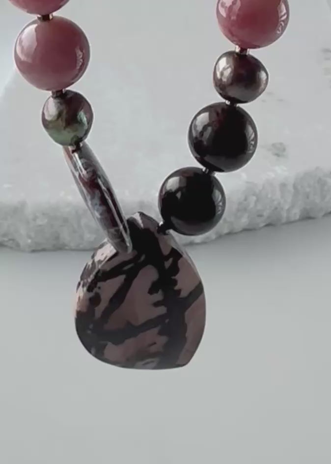 Designed and made in Canada, this Asymmetrical One-Of-A-Kind 19.5” Necklace features a beautiful mix of Stones, a Pendant of Outback Jasper, an Ocean Jasper Square, Mahogany Obsidian, Morango Quartz, Pyrite, Rhodonite and Warm Brown Pearls. This piece is finished with Gold-plated Hematite accents and a Magnetic Clasp for Secure, Easy Wear.