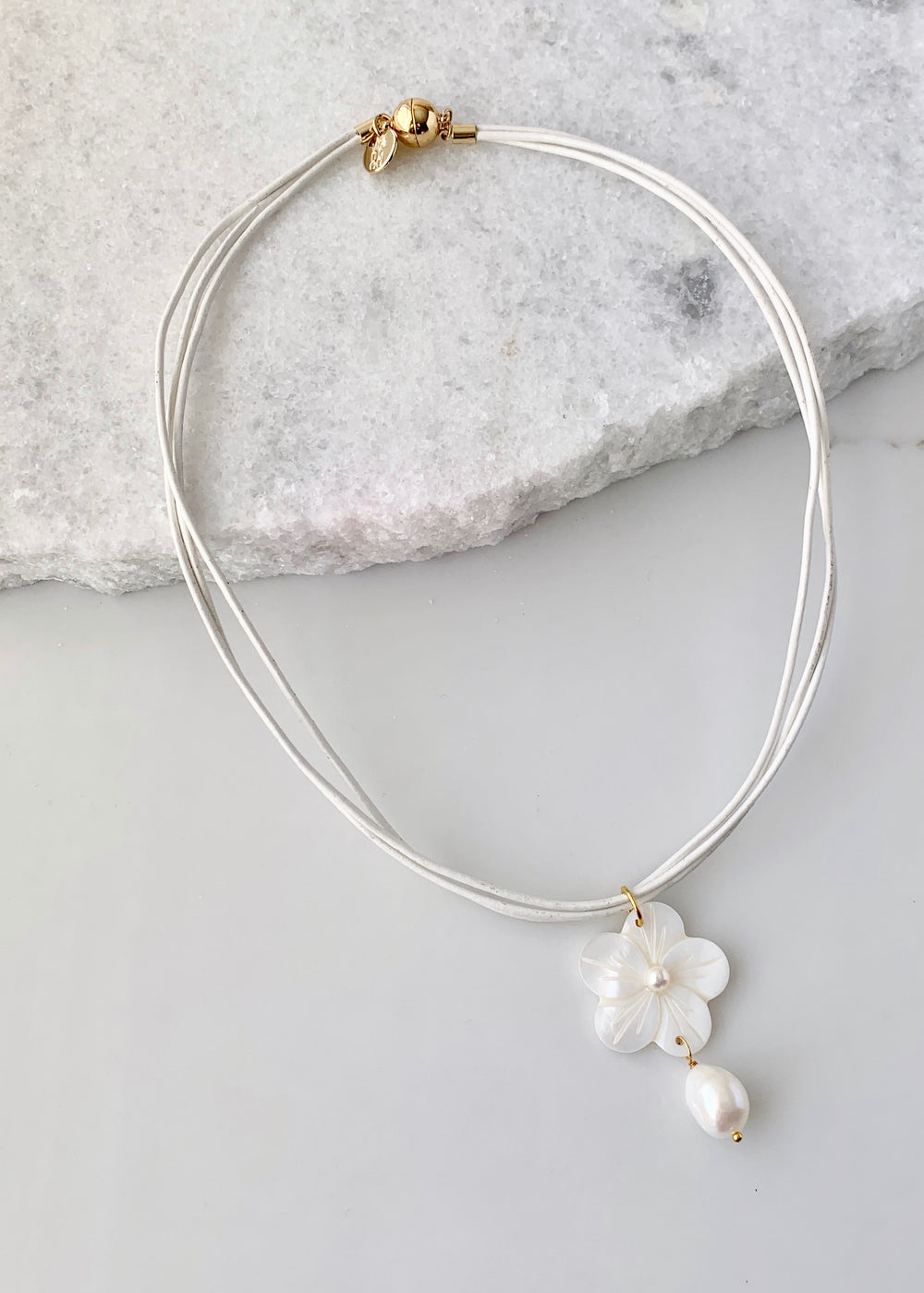 A carved shell flower and pearl pendant fall from three Strands of White Leather.  Gold accents are completed by a Strong, Secure Magnetic Clasp to ensure Easy Wear.