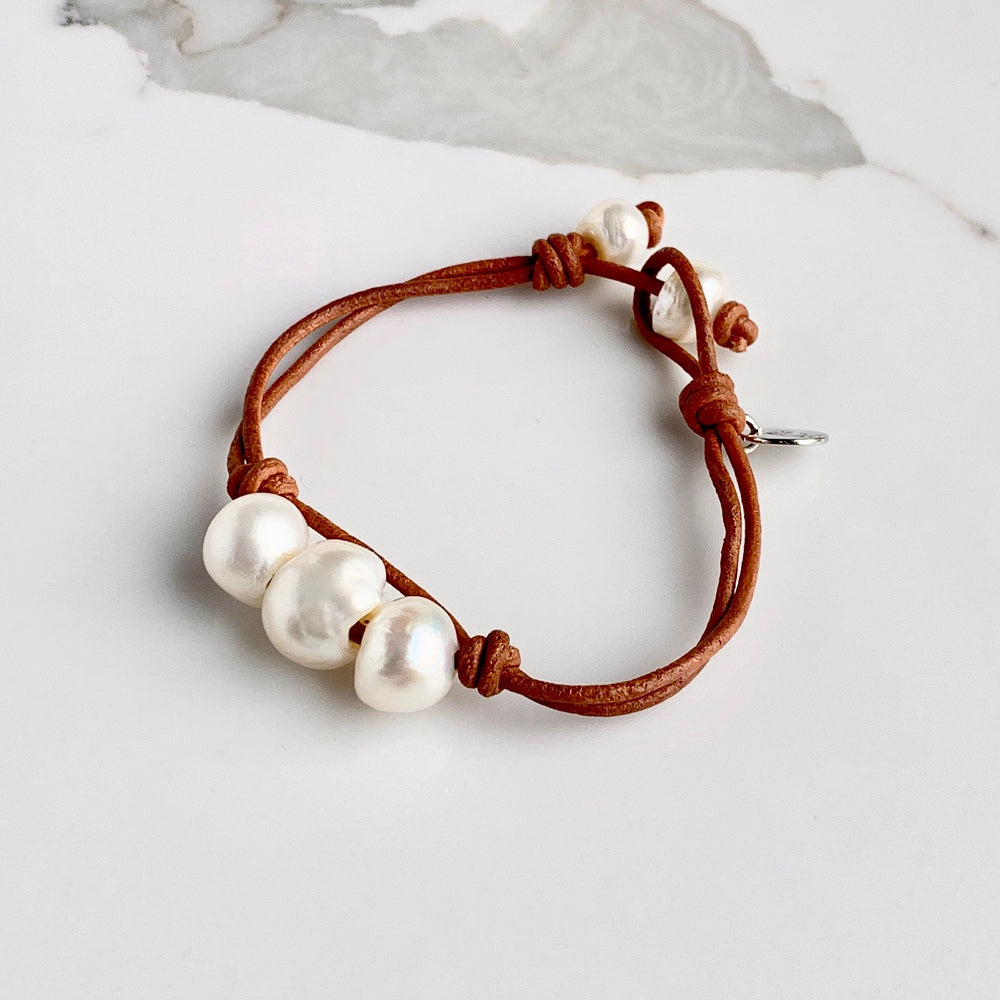 
                      
                        Tan Leather Bracelet Highlighting Three White Baroque Freshwater Pearls with a Separate Pearl and Loop Closure. Can be worn Separately or Layered with other Bracelets.
                      
                    